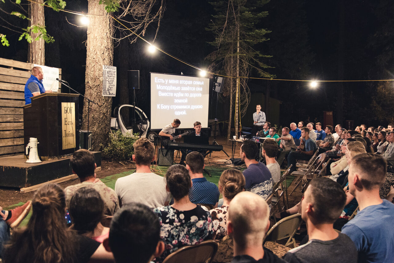 Evening outdoor worship under tall pine trees